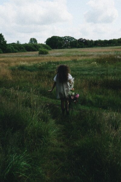 A woman running through a field wearing a dress and holding flowers