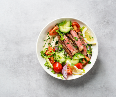 Layered salad jar filled with grains, tomatoes, avocado, greens, and cheese, surrounded by fresh vegetables, representing balanced whole-food meal prep.