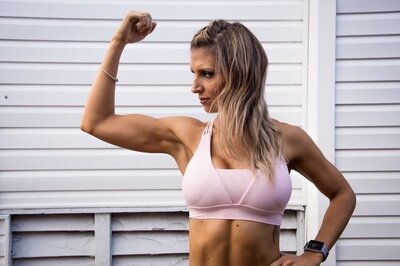fit woman in pink sports bra flexing her arm and looking at her biceps muscle