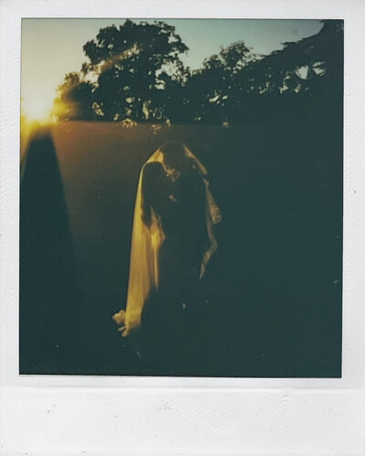 A bride and groom share an intimate moment in silhouette under the veil at sunset captured in polaroid by a Wilmington wedding photographer