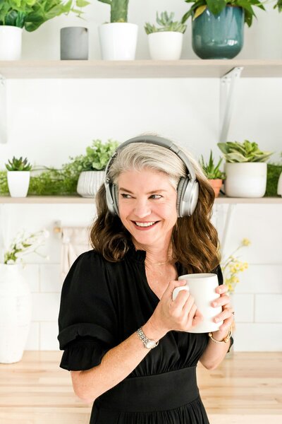 women with headphones on smiling and holding a mug