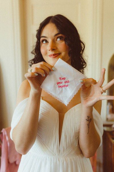 Bride smirks at camera holding kerchief that say "hold your shit together" timeless portrait at a Kansas City, MO, wedding.