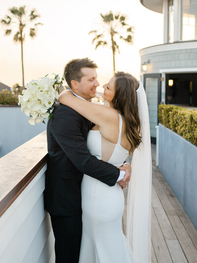 Bride and groom embrace at sunset on the Topside Roof Deck at Lido House, Newport Beach, with palm trees in the background