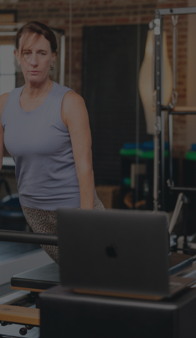woman working out on a reformer with a laptop in the foreground 