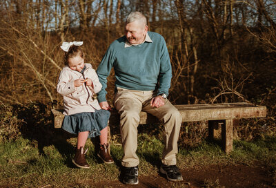 A little girl sat on a bench with her grandad, they are both smiling