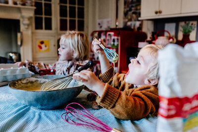 A little boy eating the cake dough he is preparing with his sister