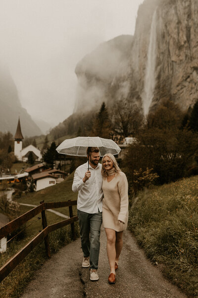 couple walking under an umbrella in rainy Lauterbrunnen, Switzerland during their engagment session