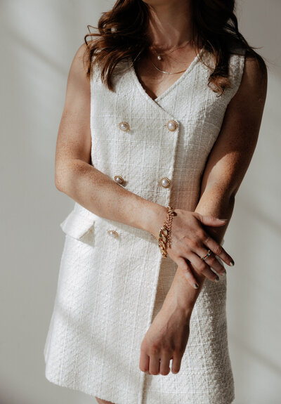 A stylish woman in a textured white dress holding her wrist, captured in soft, natural light for a timeless branding session.