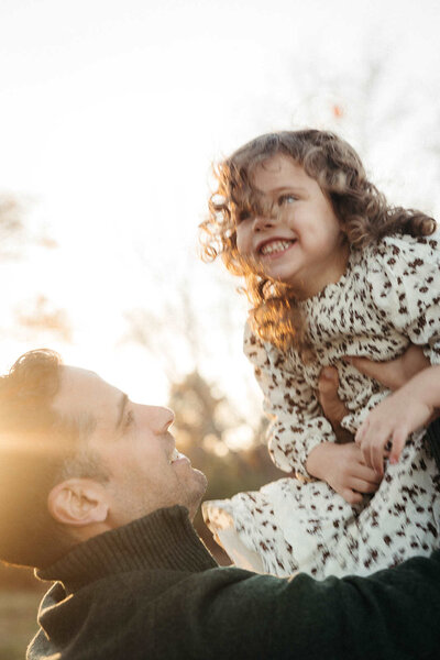 A dad holding up young daughter during a mini family photo session in Boston