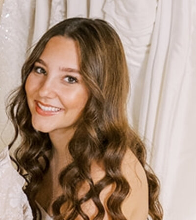 Bridal Stylist, Kaylee headshot in front of wedding dresses.