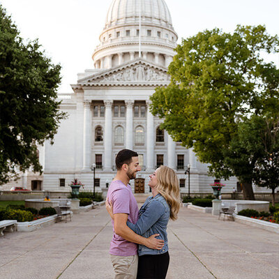 Couple smiles at each other in front of the Capitol Building in Madison, Wisconsin.