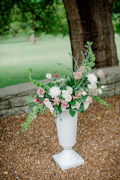 White trumpet vase filled with greenery, white and pink flowers in a whimsical design