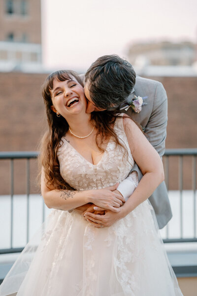Groom kissing laughing bride’s cheek