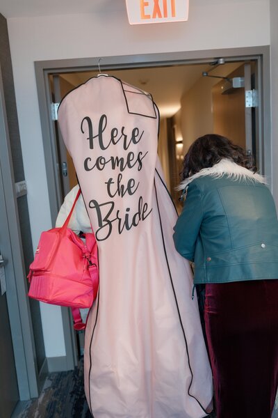bride is leaving the hotel on her way to the wedding venue with her dress in the dress bag with her mom
