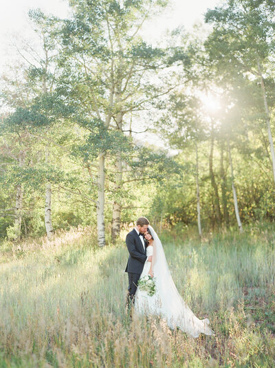 a bride and groom embracing in a field with the sun shining through aspen trees