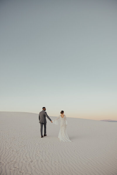bride and groom holding hands on sand dune
