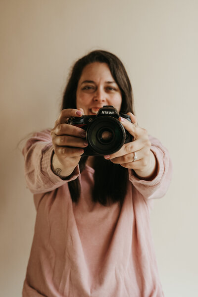 Photo of a brunette in a pink sweater pointed a camera towards the photographer