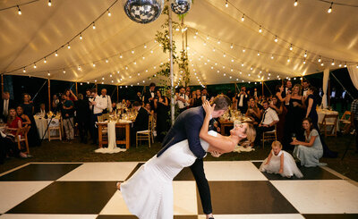 Groom dips bride during first dance and smiles at crowd watching.