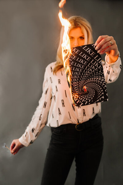 Sarah Klongerbo holding a magazine page that she lit on fire with a match