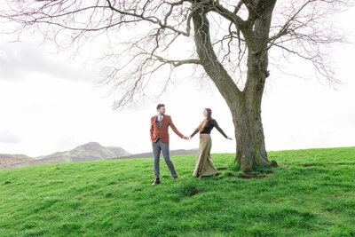 bride and groom hold hands on walk on hill top