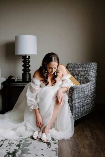 A person in a wedding dress sitting down and putting on heels 