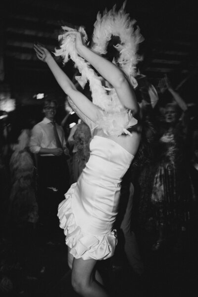 Black and white of bride dancing in short dress with white feather boa at reception