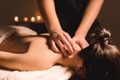 Massage therapist performing a back massage in a peaceful, candlelit room.