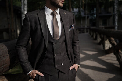 A man in a three-piece suit, hands in pockets, gazing into the distance. Monochrome tones emphasize sharp tailoring and confidence.
