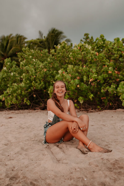 a photo of a young girl who is sitting on a beach in Costa Rica on a empty beach with a green grassy backdrop