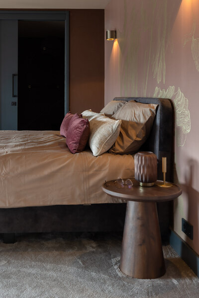 Luxe hotelkamer met beddengoed en kussens en een houten nachtkastje. Muren zijn gedecoreerd met veel oog voor detail en kwaliteit.