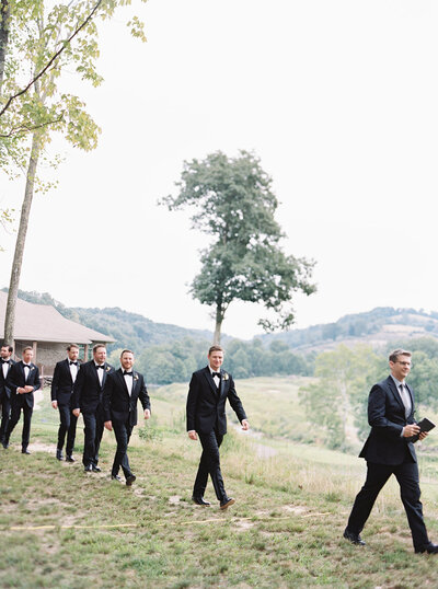 Candid moment of groomsmen walking through open field during Virginia wedding, captured by a Washington DC Wedding Photographer.