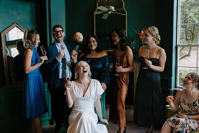 Bride drinks champagne with her bridesmaids laughing prior to the wedding ceremony.