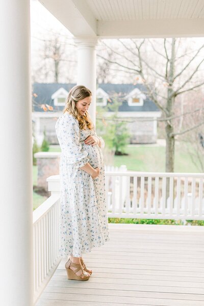 An mother stands on a porch in a maternity photo by Indianapolis maternity photographer Katelyn Ng