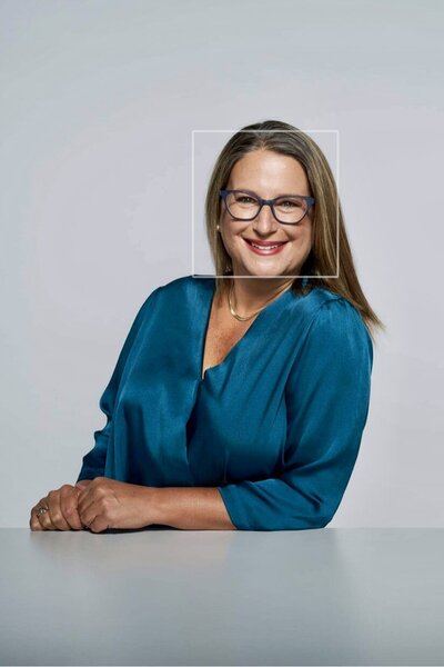 woman with blonde hair and glasses smiling while leaning her elbow on a desk