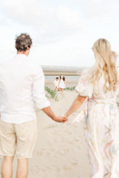 Parents facing away in foreground, with children running towards them in background on the beach near Yeppoon