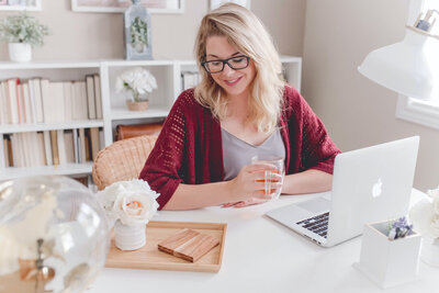 This shows a woman sitting on her desk happy to talk with ATamez Design for her discovery call, ready to book her graphic design monthly package