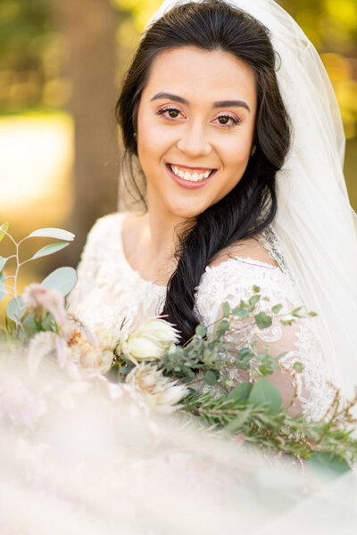 bride smiling at camera with veil and flowers
