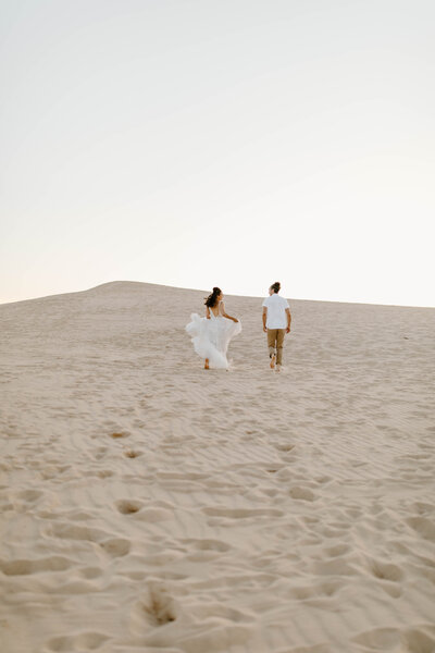 woman and man running through sand dune