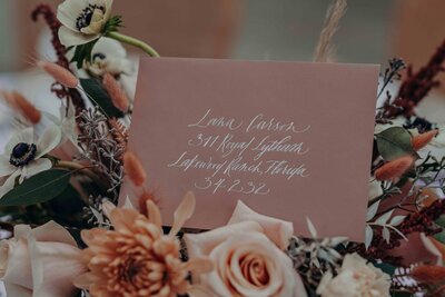 a dusty rose envelope written in calligraphy tucked into a bouquet of pale pink roses