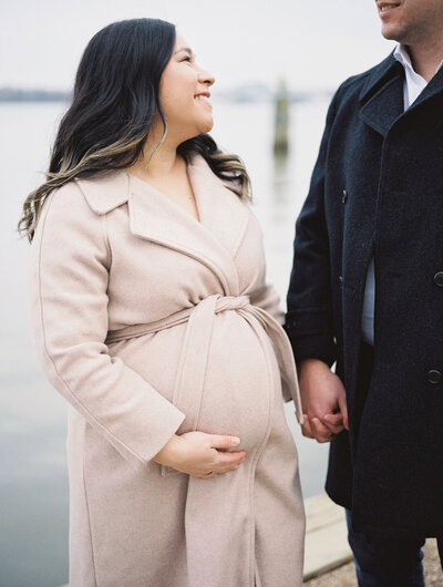 Photo of an pregnant mother in a brown trenchcoat holding  her husbands  hand by Richmond  VA Family Photographer Jacqueline Aimee Portraits