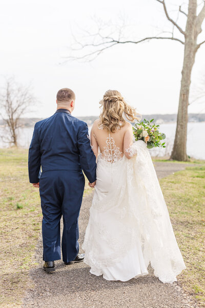 Newlyweds hold hands and walk down a small path to a lake