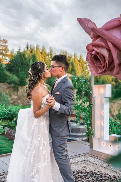 Romantic photograph capturing a bride and groom sharing a tender kiss, framed by a single rose, symbolizing love and passion on their wedding day.