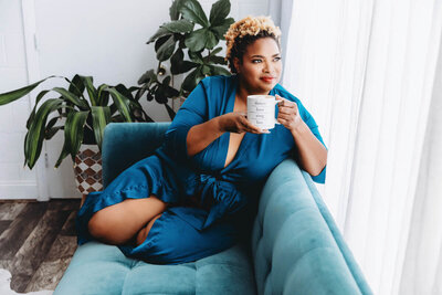 Portrait of black woman leaning against couch holding coffee mug