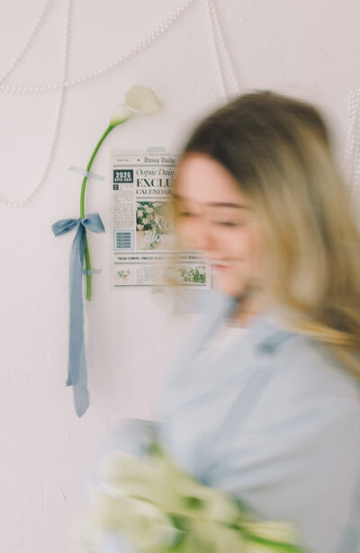 Woman in motion with a flower and newspaper taped to a white wall with pearl garlands. A whimsical branding photo showcasing blur, texture, and motion. Greenville South Carolina portrait photographer – Dani Lacey Photographs.