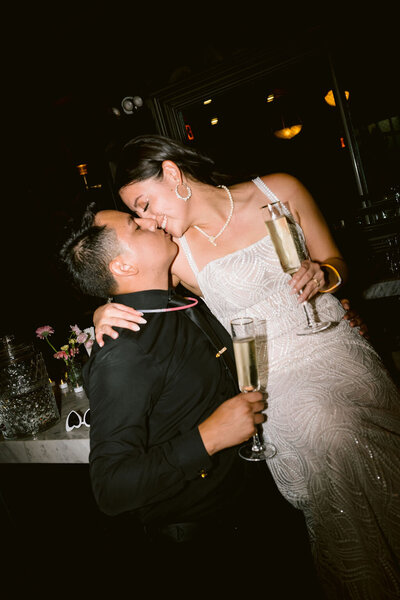 married couple going in for a kiss while holding champagne glasses