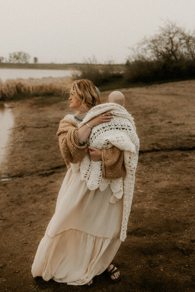 Photo of a mom holding her baby all snuggled up to her along a sand bar at the lake.