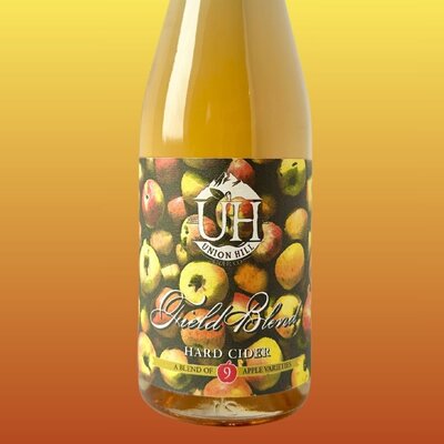 A bottle of Field Blend hard cider made by Union Hill. Label has a bunch of red and yellow apples as the background.