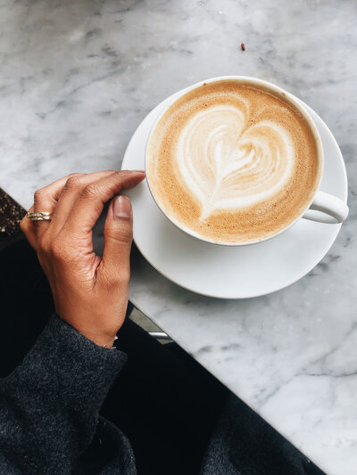 Hand touching a white mug with latte art on a counter