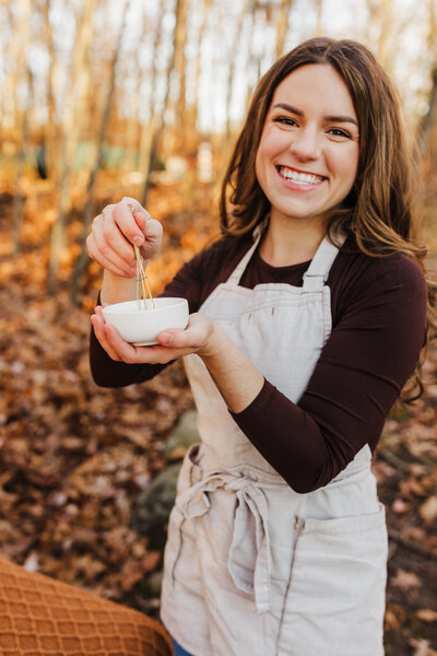 Photo of a woman holding a small bowl and whisk.