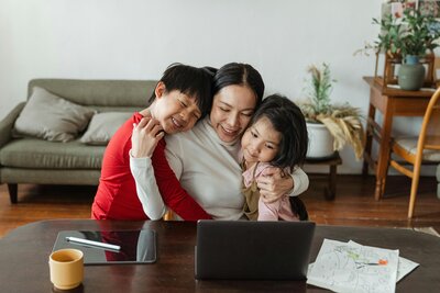 woman hugging two kids smiling at the computer